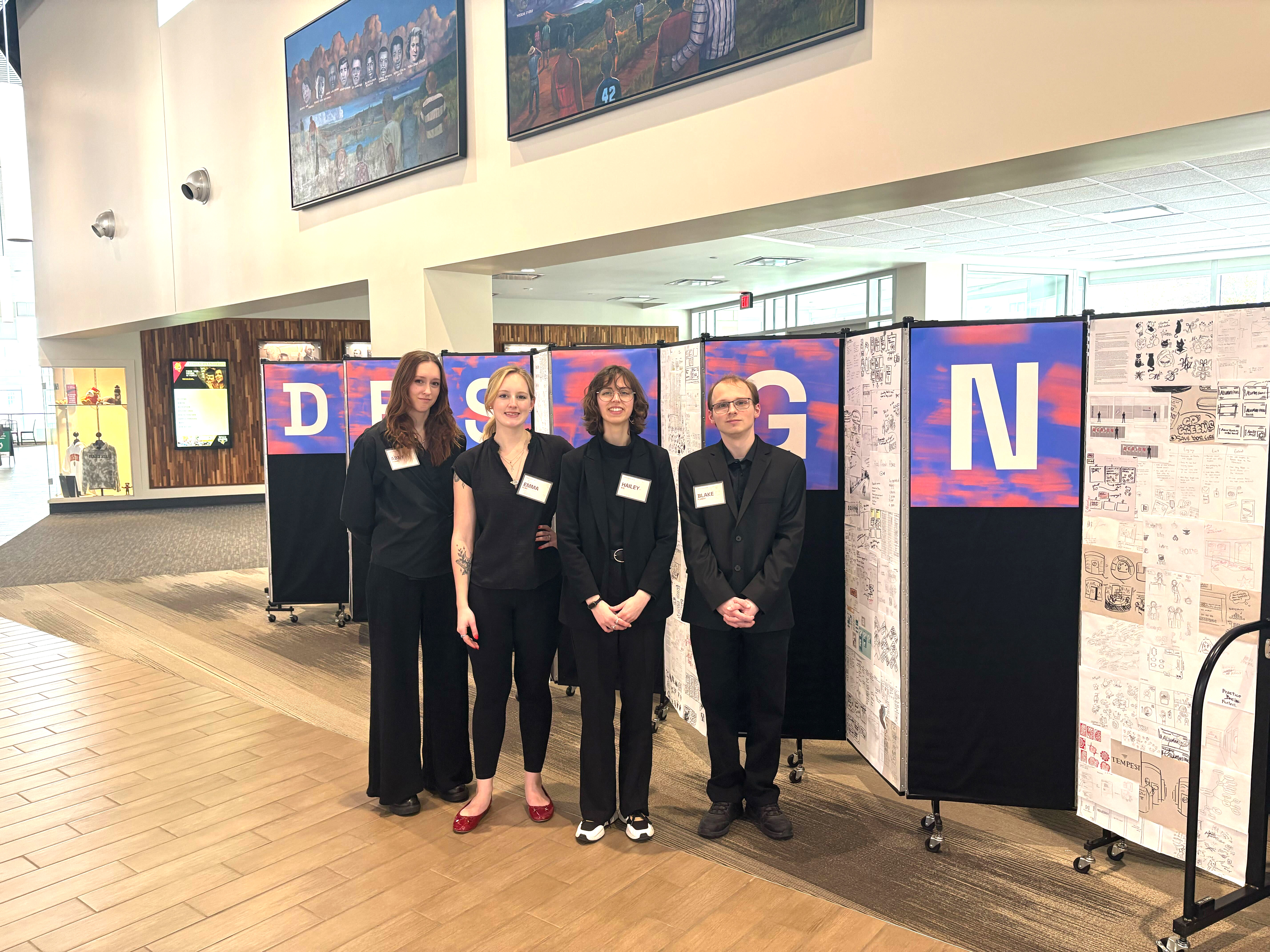 Abby Keown, Emma Eling, Hailey Nye, and Blake Flanery posed in front of a zig zagging board featuring process work and the word DESIGN in bold letters