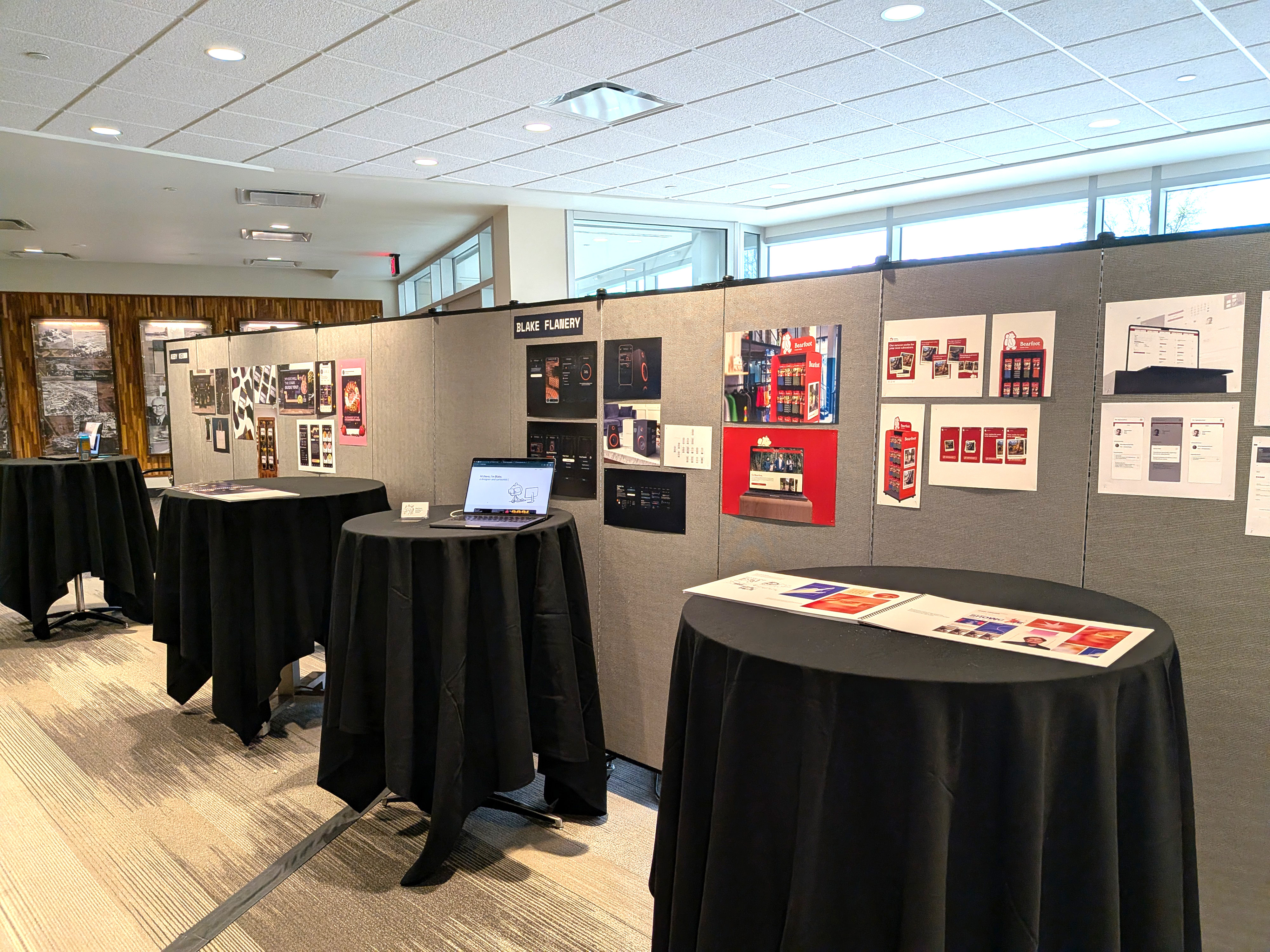 A wide shot of senior work pinned to a grey wall near tables drapped with black fabric