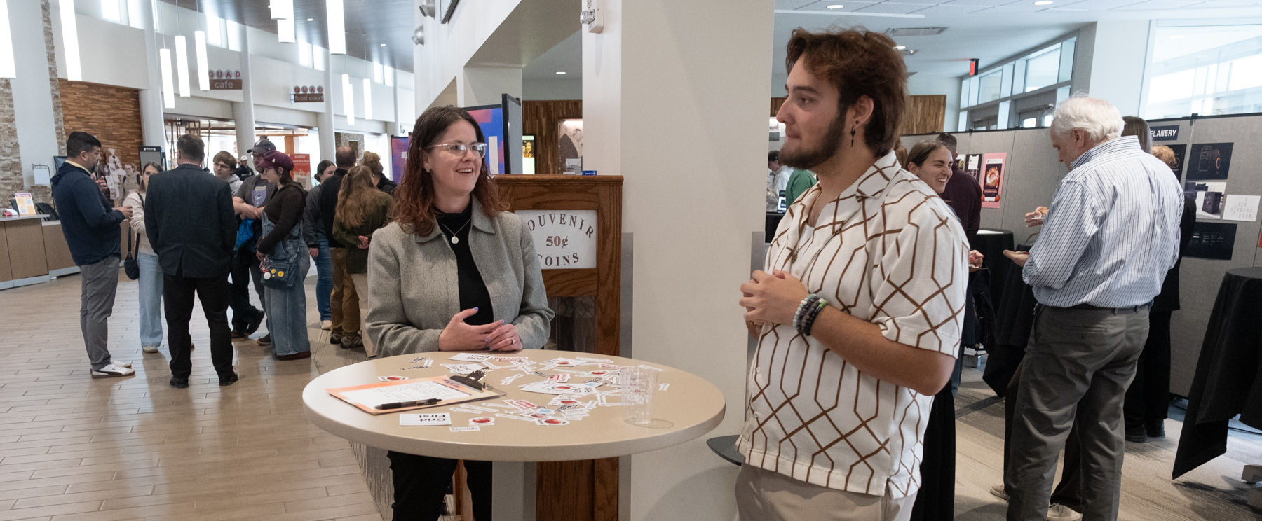 Gary Babcock speaking with a woman at a tabel full of stickers with a crowd of people in the background
