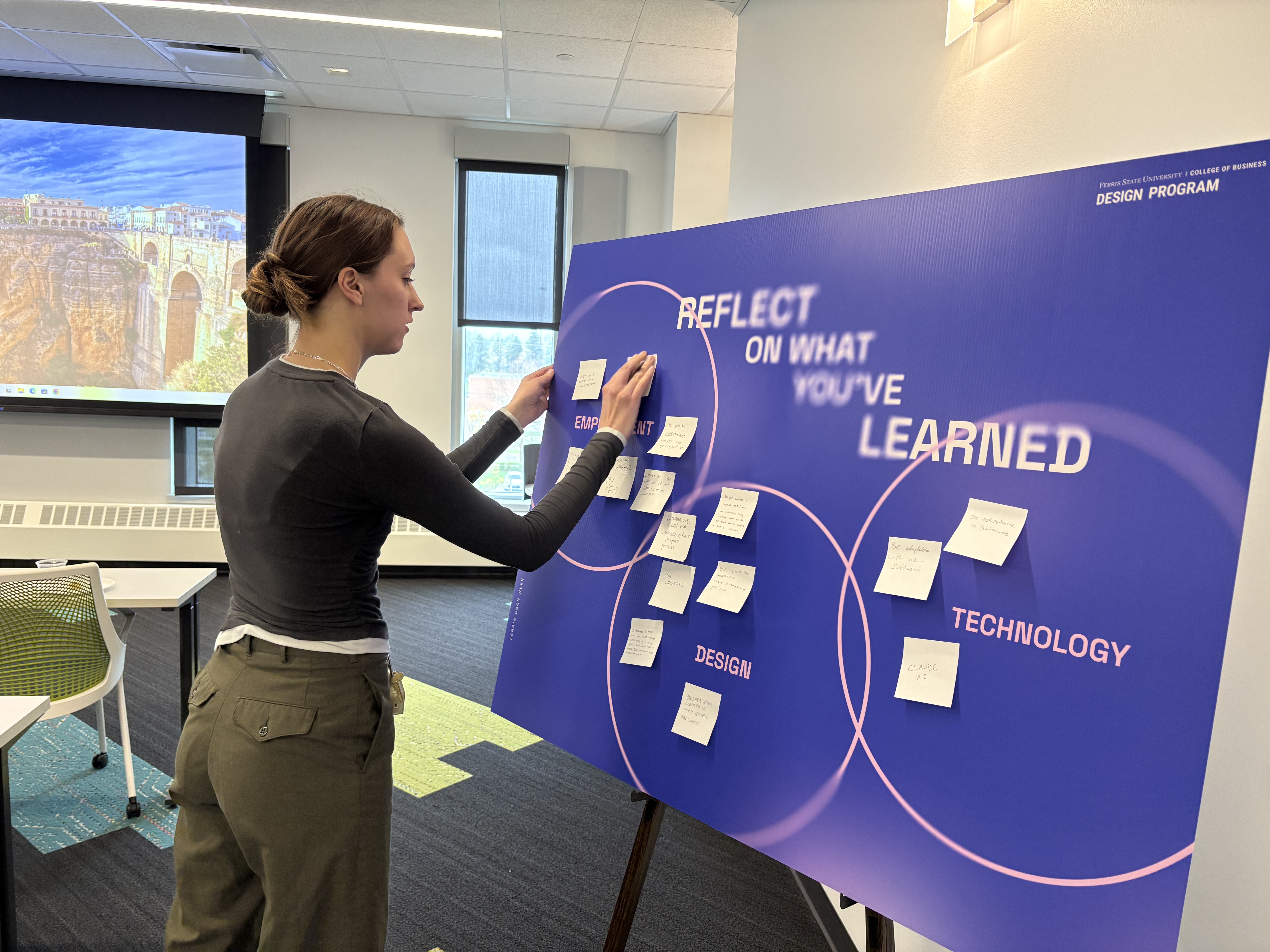 Abby Keown putting a sticky note onto a blue and pink board full of information gained from the panel